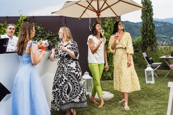Gruppe von Gästen mit Getränken beim entspannten Empfang im Garten unter Sonnenschirmen.