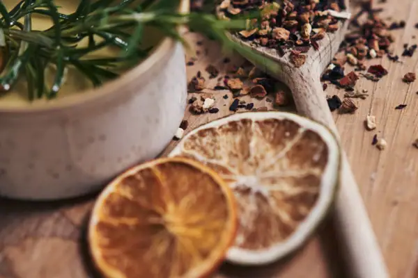 Ein Löffel mit Gewürzen, Zitrusfrüchten und eine Schüssel mit Öl auf einer Holzoberfläche.