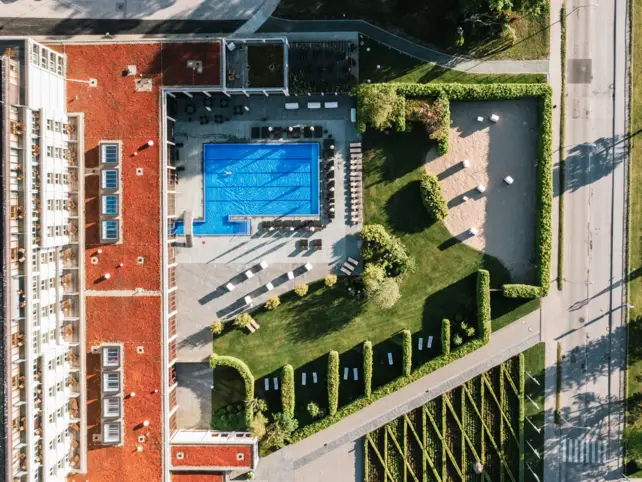 Piscina esterna con edificio circondato da strada e alberi.