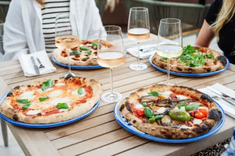 Gruppo di pizze su un tavolo con bicchieri di vino.