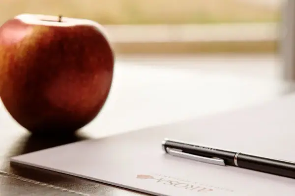 Penna su un foglio di carta accanto a una mela.