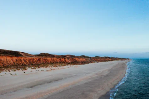 Spiaggia sabbiosa con un corpo d'acqua e colline sullo sfondo.