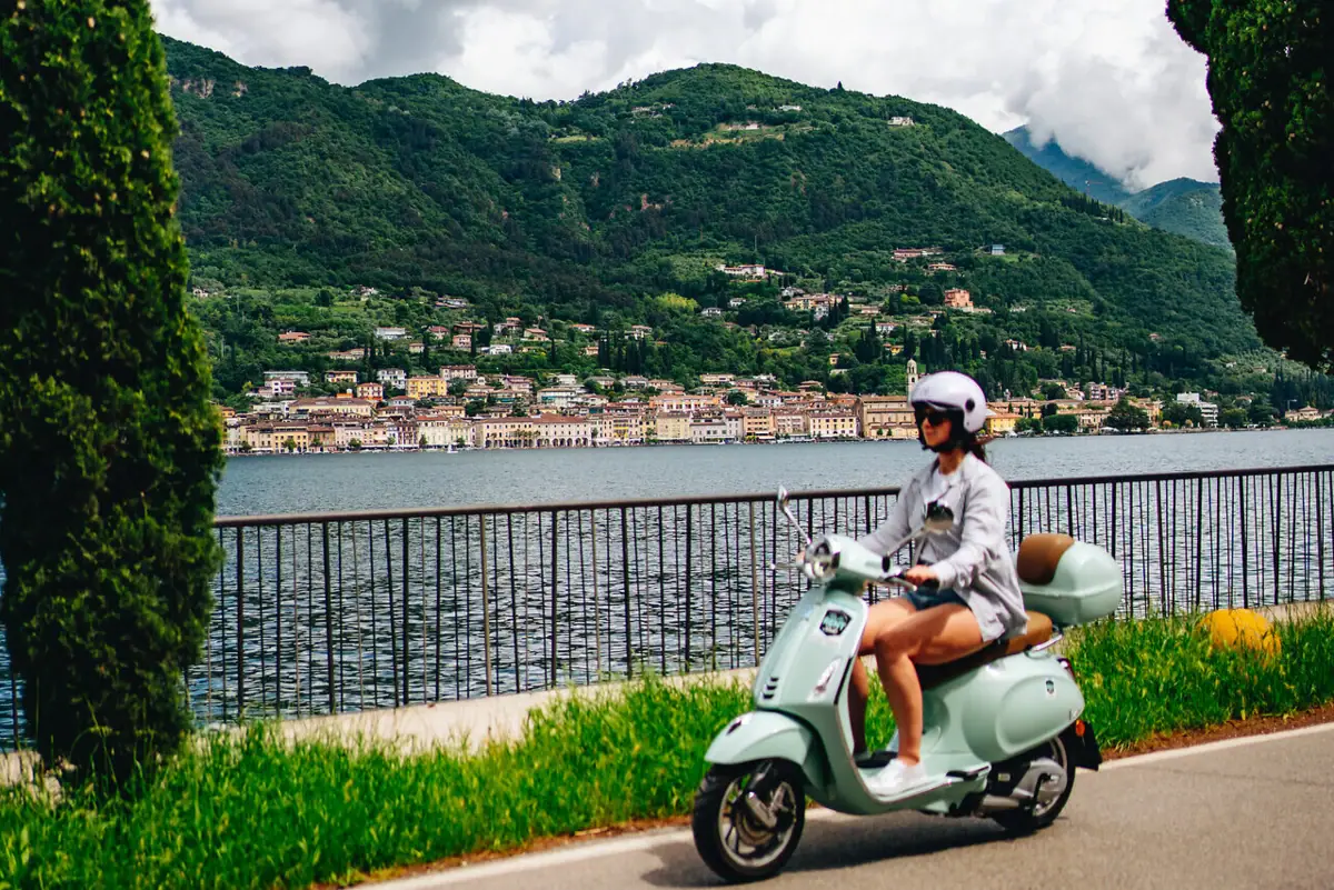 Lago di Garda Una donna sta guidando uno scooter su una strada che costeggia un corso d'acqua.