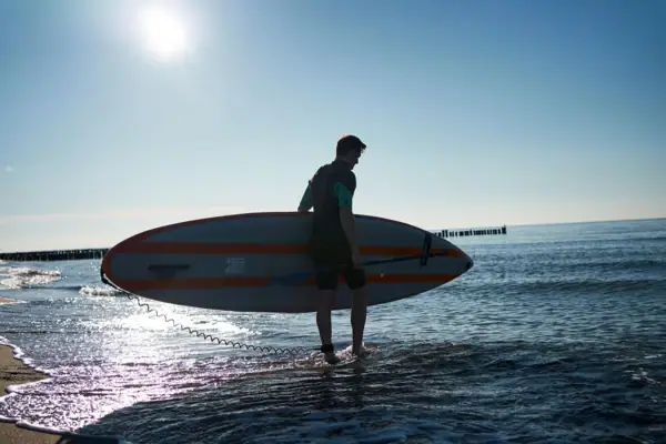 Ein Mann trägt ein Surfbrett im Wasser.