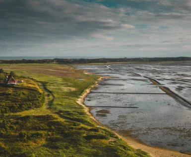 Paesaggio con spiaggia e campo erboso sotto un cielo nuvoloso.