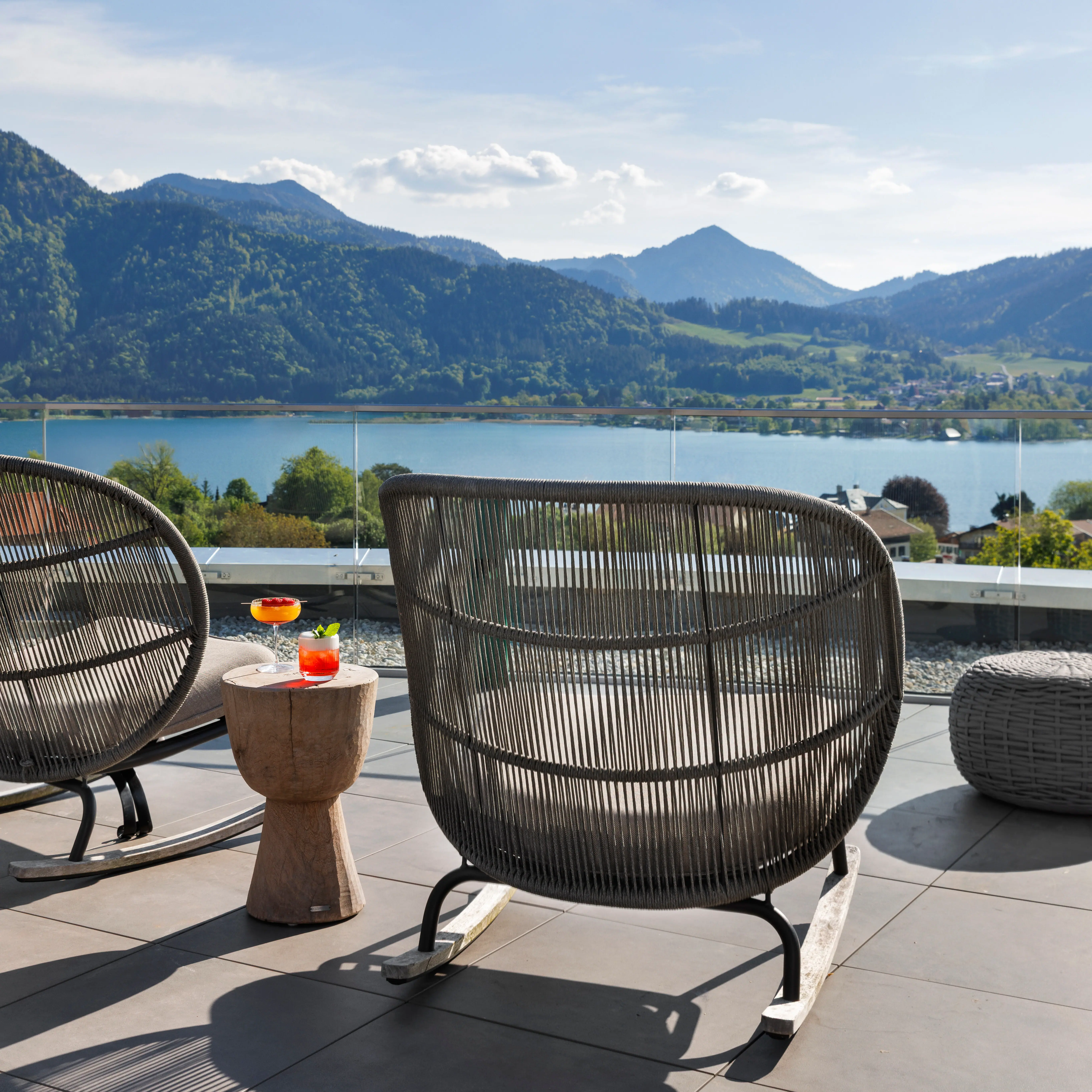 La terrazza dell'A-ROSA Tegernsee con poltrone e bevande e una vista spettacolare sul lago Tegernsee e sulle montagne.