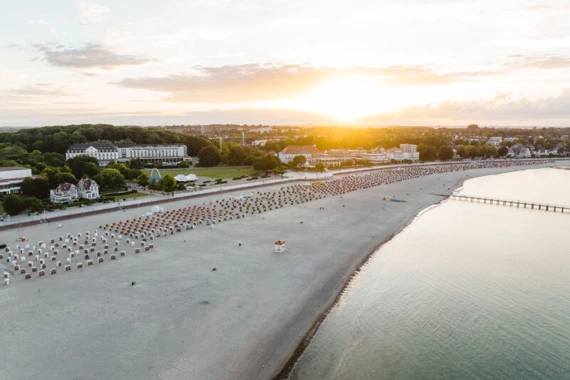 Spiaggia affollata con numerosi ombrelloni e persone, sotto un cielo parzialmente nuvoloso.