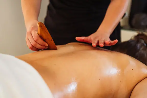 Eine Person massiert mit einem Massagegerät den Rücken einer anderen Person.