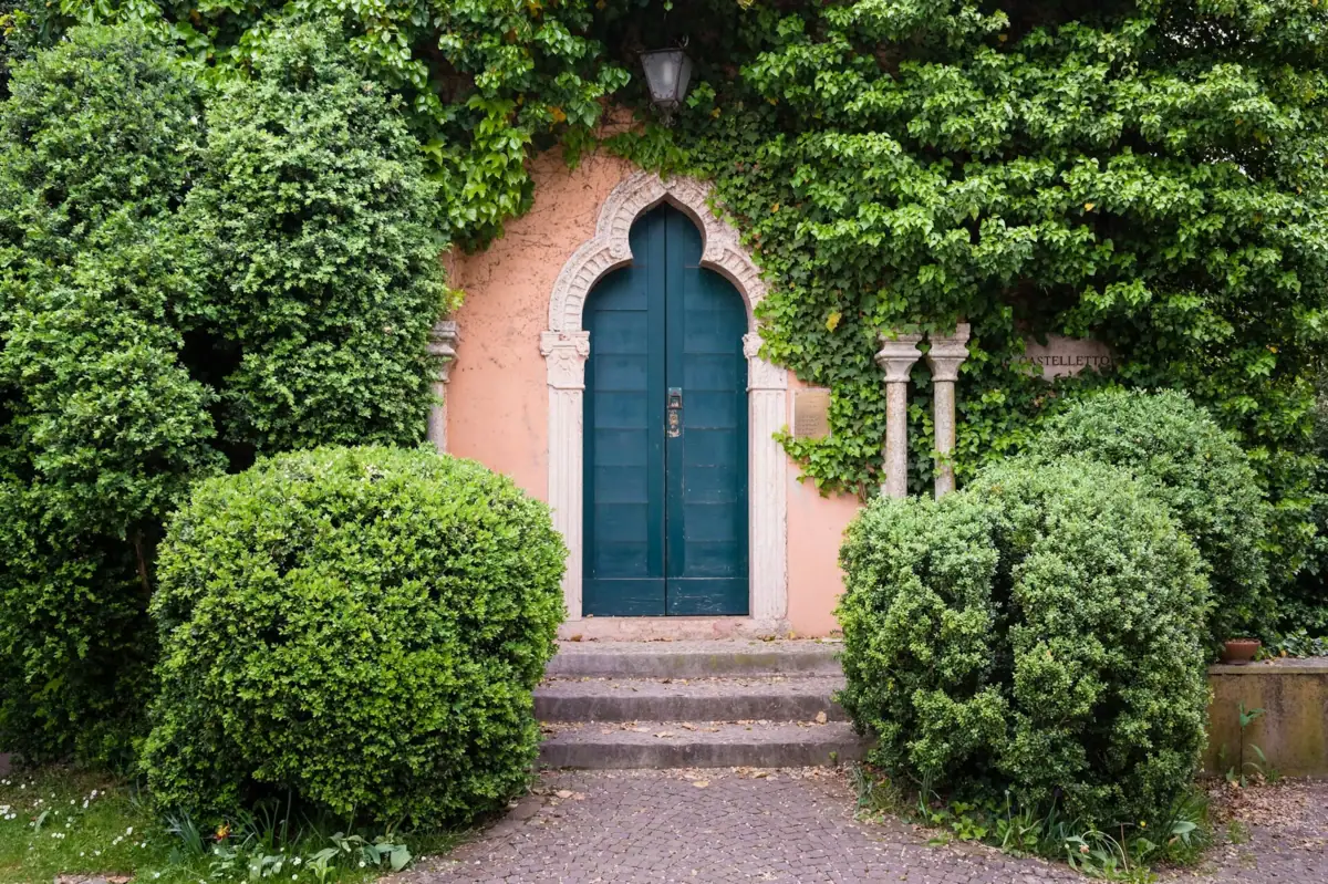 PORTA Tür mit Steinbogen und Steinweg, umgeben von Büschen.