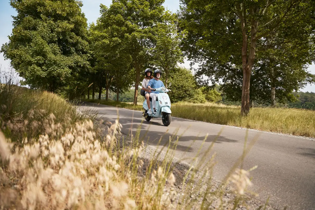 Ein Mann und eine Frau fahren auf einem Roller eine Straße entlang.