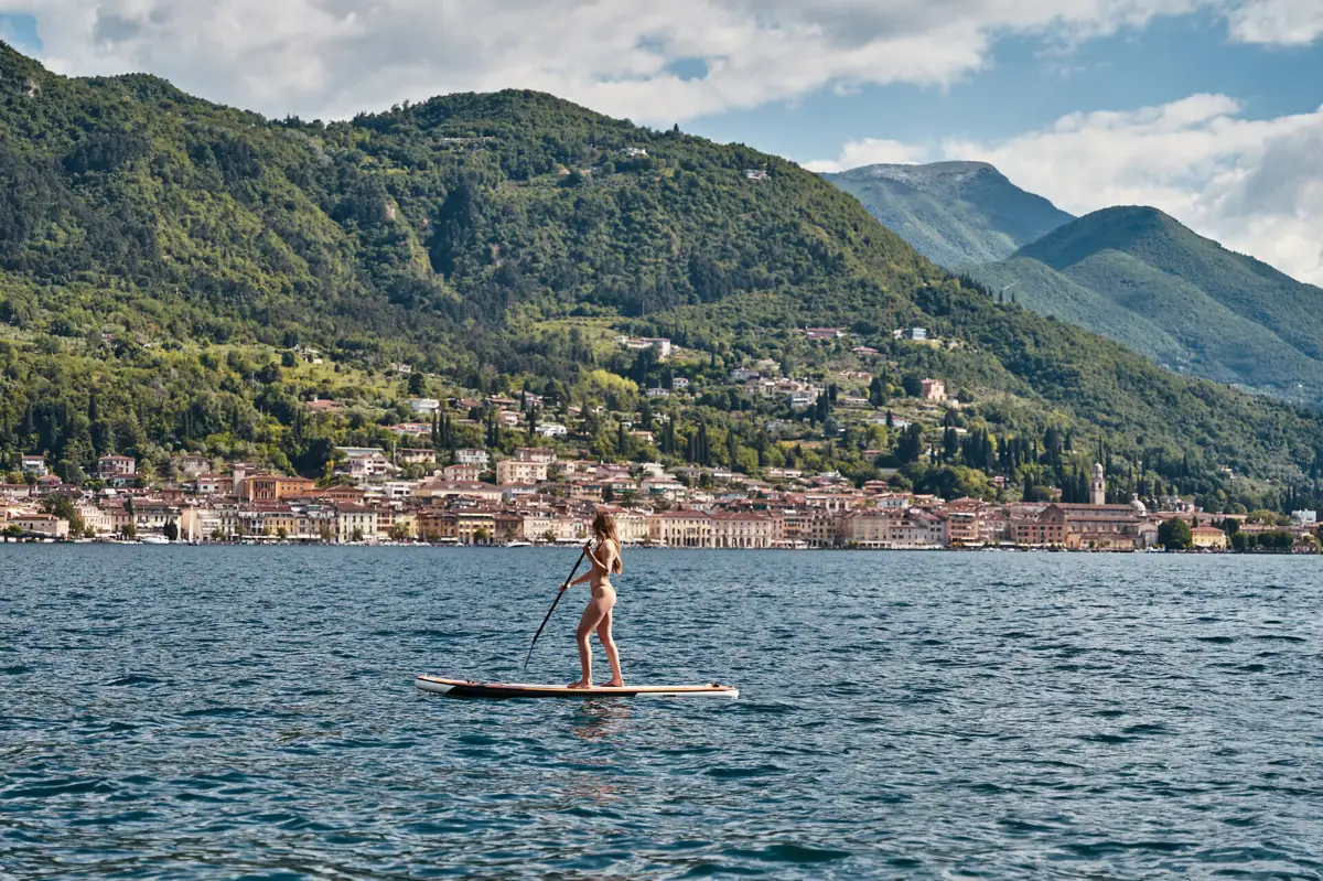 SUP sul Lago di Garda Una donna su una tavola da paddleboard in acqua, con una città sullo sfondo.
