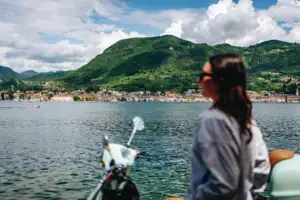 Eine Frau sitzt auf einem Roller und blickt auf ein Gewässer.