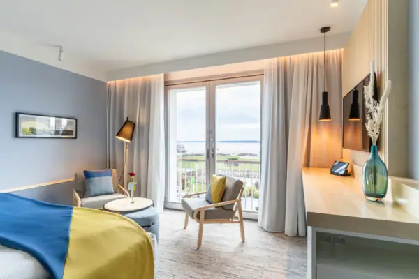 Hotelzimmer mit Bett, Tisch und Stühlen sowie einem großen Fenster mit Blick auf die Ostsee.