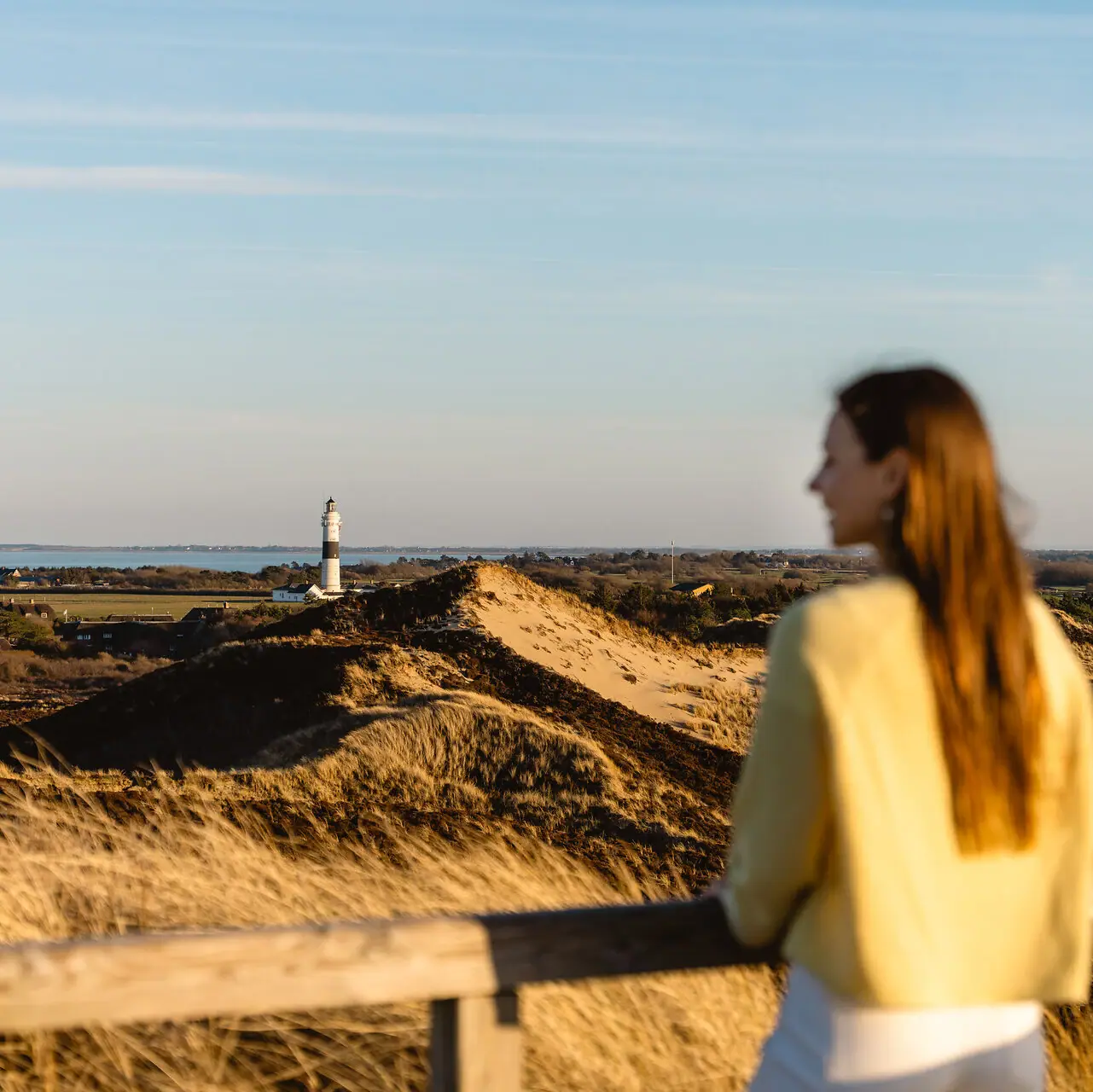 Una donna è in piedi su una recinzione e guarda un faro sull’isola di Sylt.