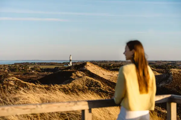 Una donna si trova sulla duna Uwe a Sylt e guarda un faro.