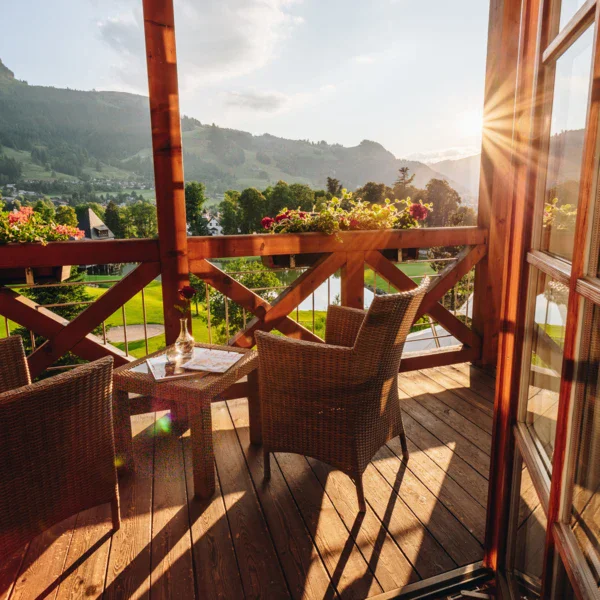 Terrazza soleggiata con tavolo e sedie, circondata da montagne e vegetazione.