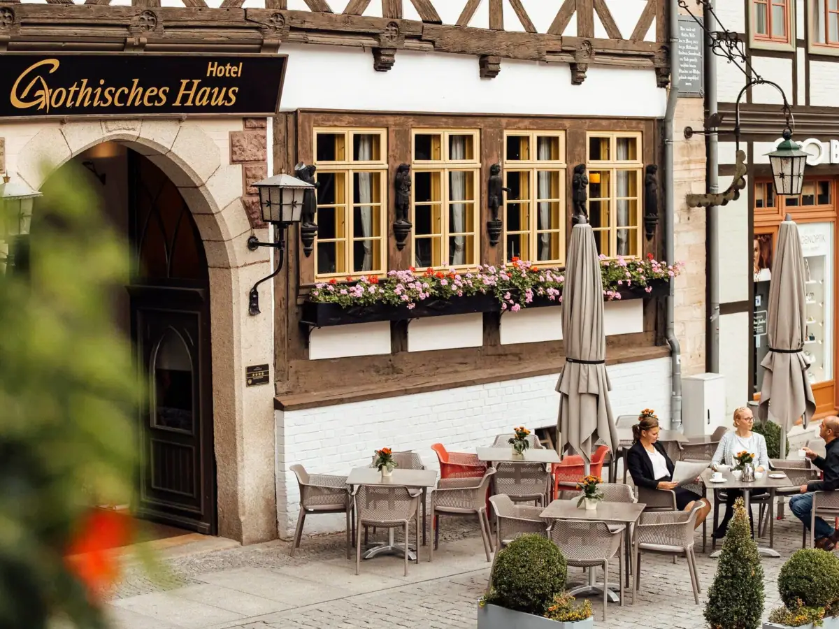 Gothisches Haus Terrasse Eine Gruppe von Menschen sitzt an Tischen im Freien vor einem Gebäude.