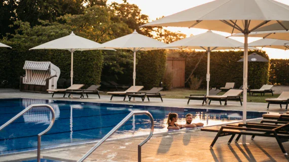 Gruppo di persone in una piscina all'aperto con alberi e cielo visibili.