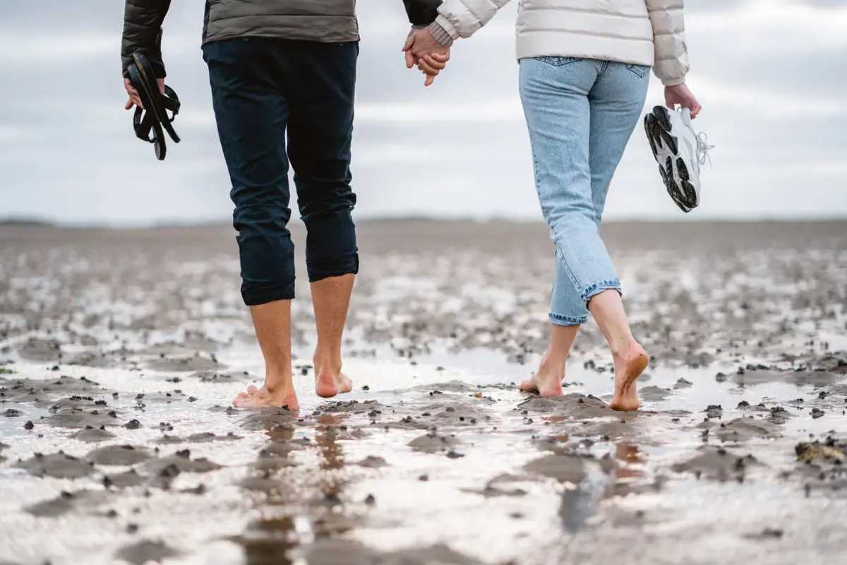 Un uomo e una donna, tenendosi per mano, fanno una passeggiata nella zona delle distese fangose di Sylt.
