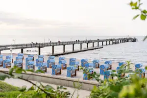 Strandkörbe am Strand mit Blick auf einen Steg und Menschen im Hintergrund.