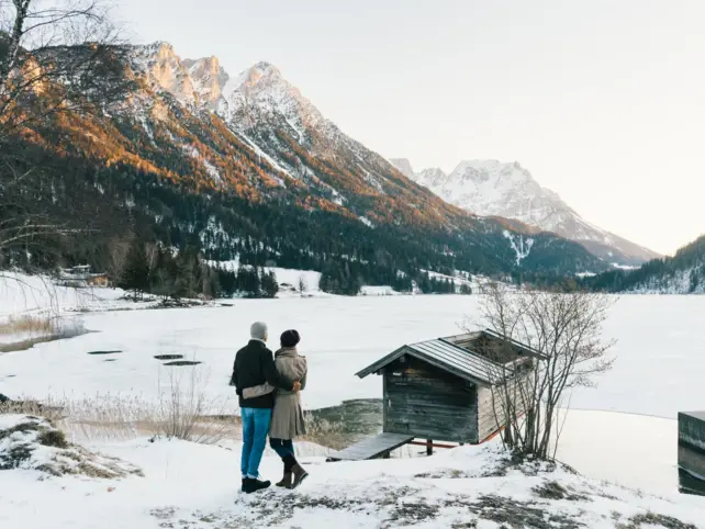 Un uomo e una donna in piedi sulla neve vicino a un lago, circondati da alberi innevati.