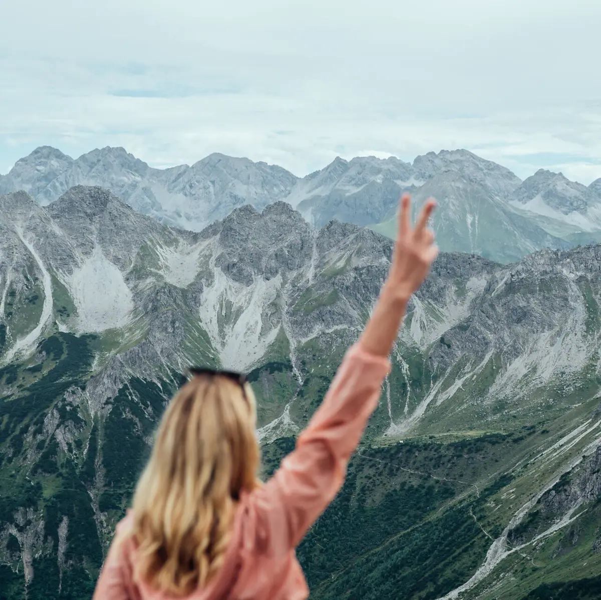 Una donna si trova su una montagna con la mano alzata.