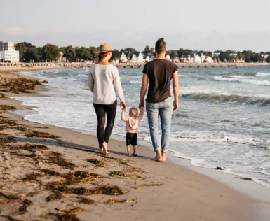 Uomo e donna che camminano tenendosi per mano su una spiaggia.