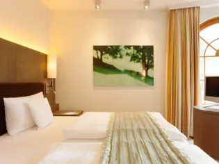 Una luminosa camera da letto con letto matrimoniale e copriletto verde.  Sullo sfondo, un quadro verde appeso alla parete e una finestra decorata con una tenda gialla.