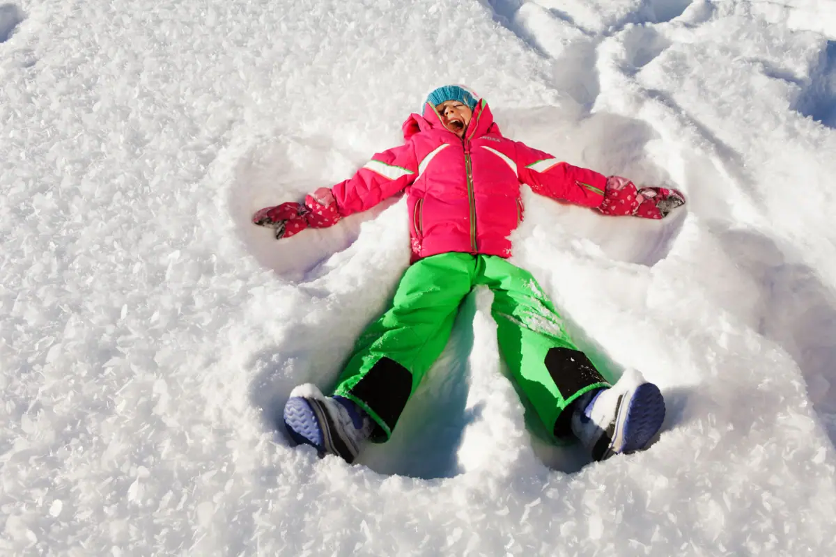 Un bambino è sdraiato sulla neve e sta facendo un angelo di neve.