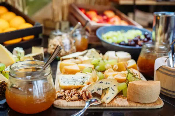 Auf einem Buffett steht ein Holzbrett verschiedenen Käsesorten, Weintrauben und Feigensenf.