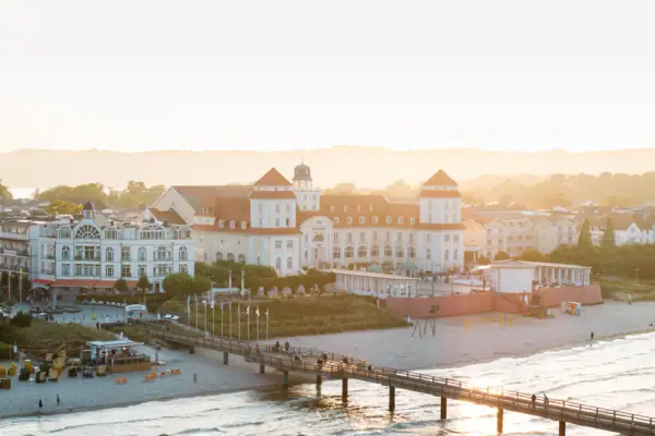 Hotel benessere Kurhaus Binz Un molo su una spiaggia, con edifici e l’acqua sullo sfondo.