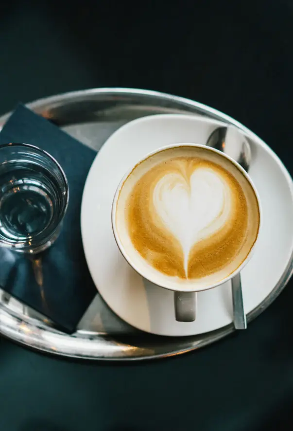 Tazza di caffè con schiuma a forma di cuore su un piatto bianco.