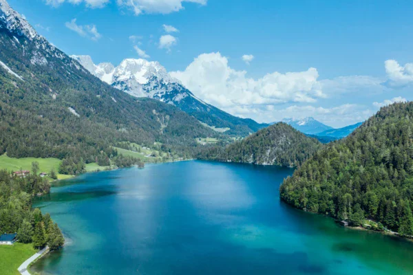 Lago circondato da montagne con alberi e nuvole nel cielo.