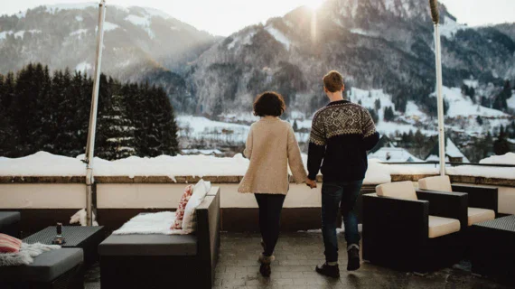 Un uomo e una donna si tengono per mano su un balcone con vista su una montagna innevata.