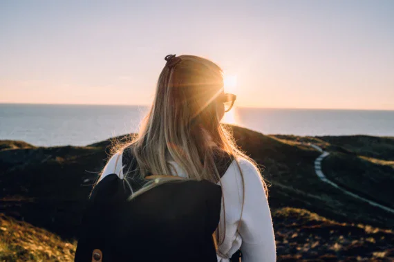 Donna in abbigliamento esterno che guarda il sole al tramonto sulla spiaggia.