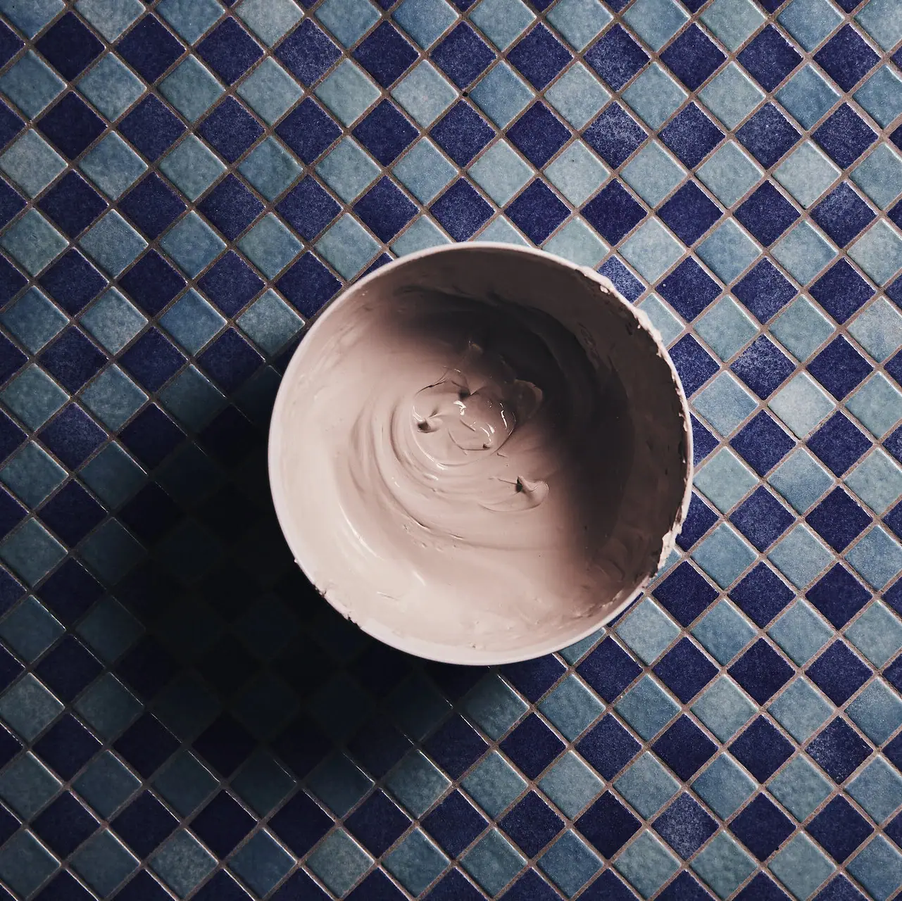 SPA-Stillleben Eine Schale mit beiger Paste auf einem blauen Fliesenmosaik
