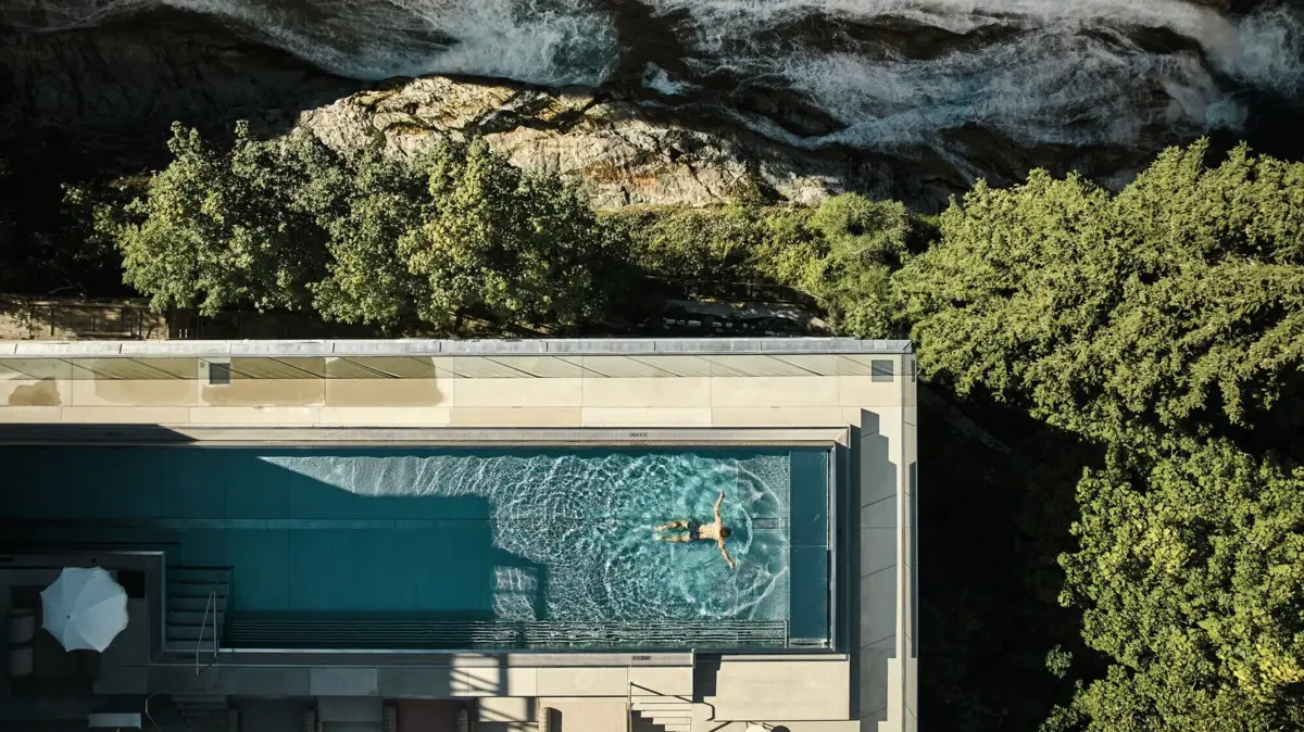 Perfektion in einem Poolbild CVogelperspektive eines Poolbildes in dem jemand schwimmt, neben einem Wasserfall, Felsen und Landschaft