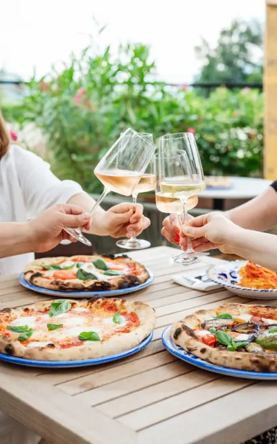 Gruppo di persone seduto a un tavolo con pizze e bicchieri di vino.