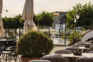 Tavoli e sedie all'aperto con alberi e una strada sullo sfondo.