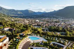 A-ROSA Hotel am Gardasee Ein Swimmingpool mit Blick auf eine Stadt, umgeben von Bäumen und Bergen.