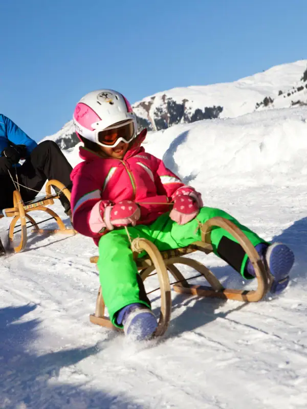 Un uomo e una bambina scendono in slittino lungo un pendio innevato.