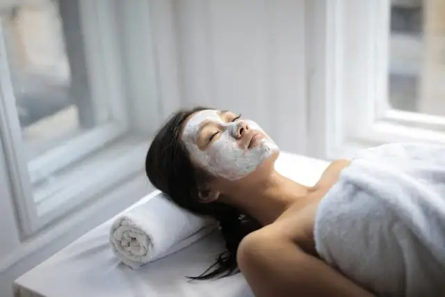 PURE Gesichtsbehandlung Eine Frau liegt mit einer weißen Maske auf dem Gesicht.