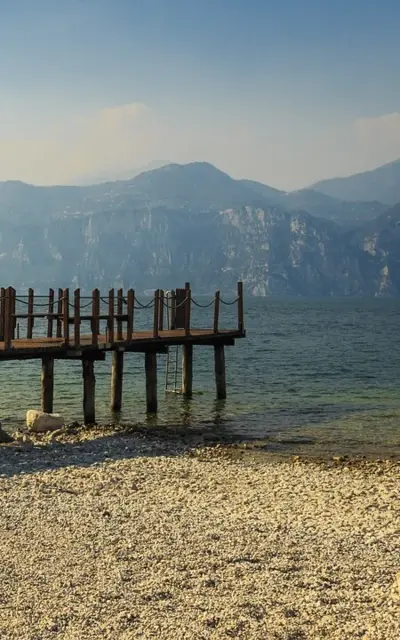 Ponte di legno su uno specchio d'acqua in un paesaggio montano nebbioso.