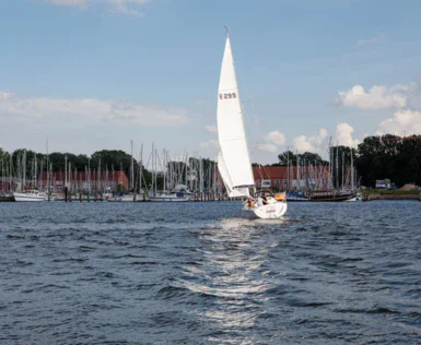 Una barca a vela naviga su un lago con cielo nuvoloso.