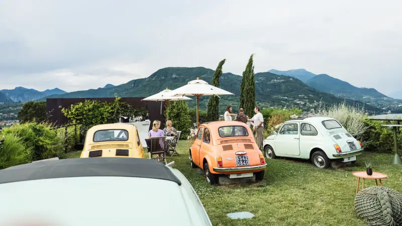 Un gruppo di auto parcheggiate sull'erba con persone intorno.