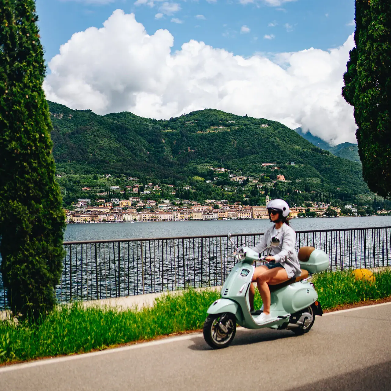 Una donna guida uno scooter su una strada vicino a un corpo d'acqua.