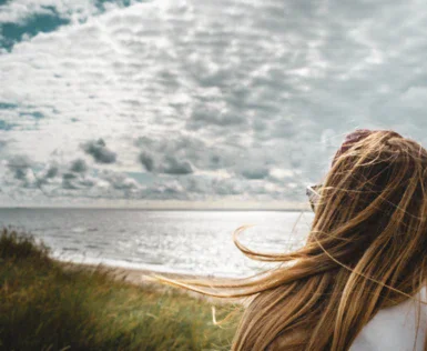 Donna con capelli lunghi in piedi su una spiaggia che guarda l'oceano.