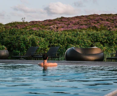 Donna in una piscina esterna con sedie e cespugli sullo sfondo.