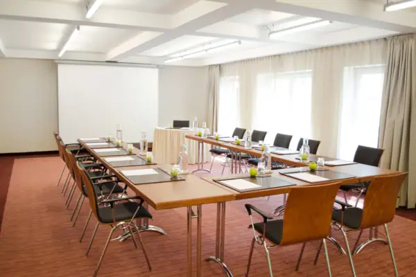 Ein Tagungsraum mit Tischen und Stühlen sowie einer Leinwand an der hinteren Wand.