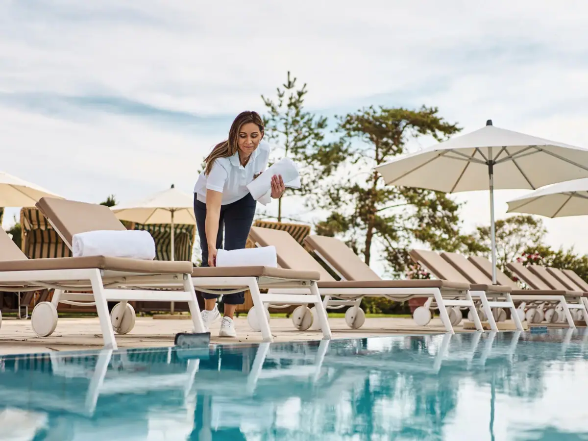 Donna che pulisce una piscina all'aperto sotto un cielo azzurro.